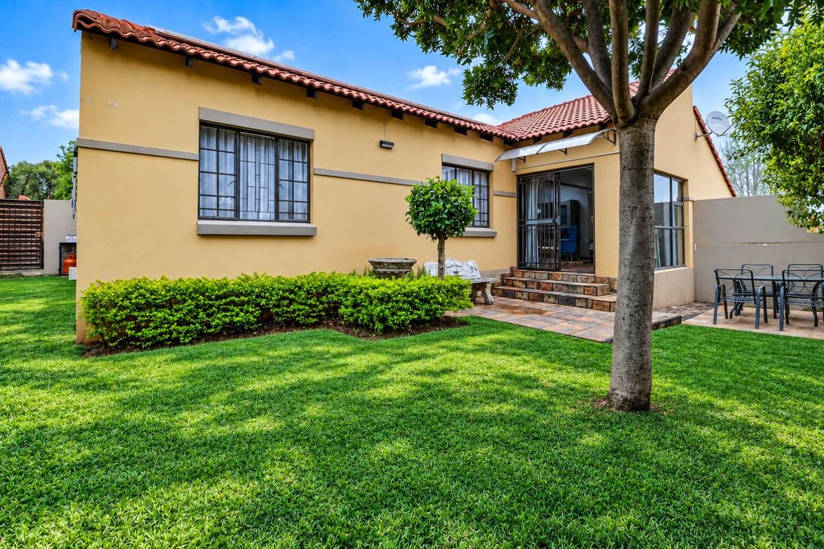 A well-maintained rear exterior view of the townhouse featuring a stone-tiled patio, landscaped garden, and terracotta roof tiles.