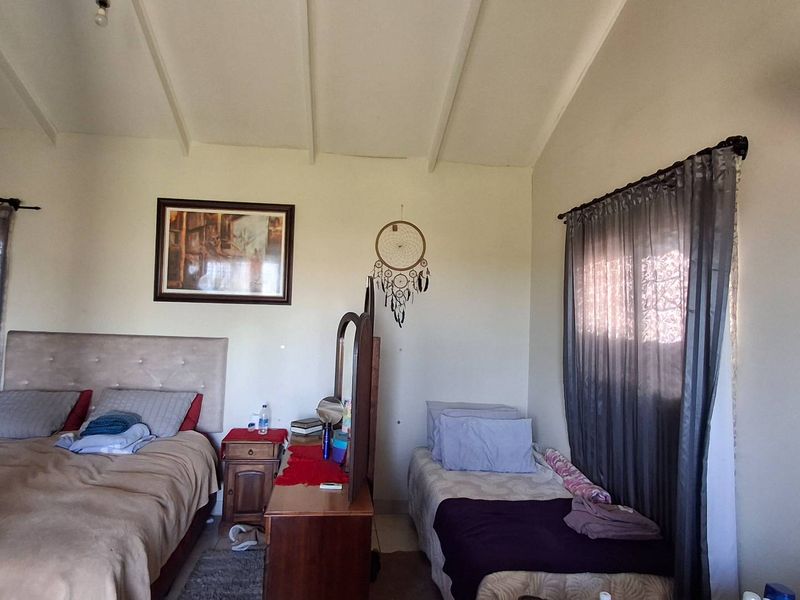 A bedroom featuring an exposed beam ceiling and a wall-mounted fan, providing a functional space with natural light from the windows.