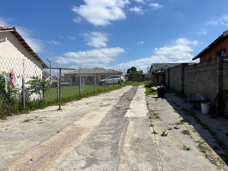 A rear exterior view showing a concrete driveway, chain link fencing with razor wire, and a concrete block boundary wall.
