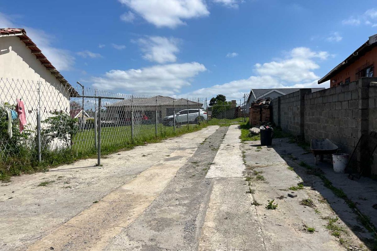 A rear exterior view showing a concrete driveway, chain link fencing with razor wire, and a concrete block boundary wall.