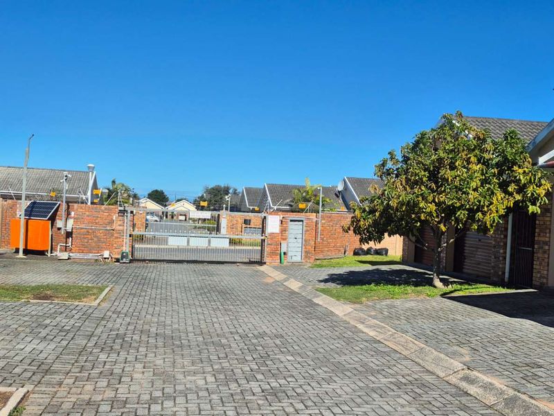 A view of the townhouse complex entrance featuring paved driveway, brick boundary walls, security gate, and multiple garage units.