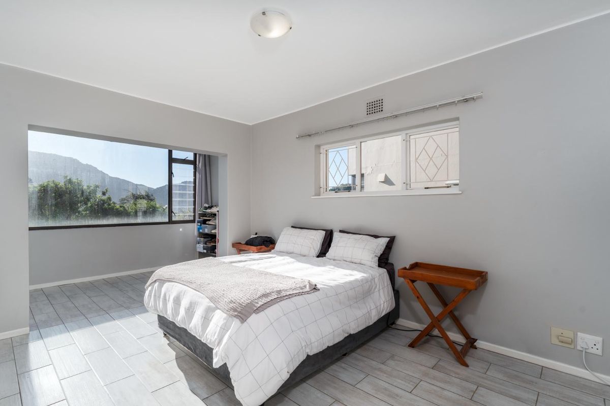 A bright bedroom featuring large windows with natural light, tiled flooring, and neutral wall finishes.
