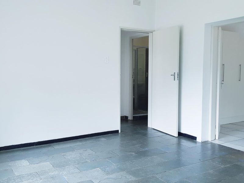 An empty bedroom featuring stone tile flooring, built-in cupboards, and neutral white walls, offering a blank canvas for personalization.