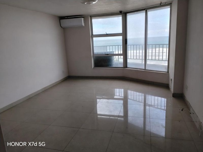 An empty, tiled living room featuring a split-system air conditioner and large windows with direct ocean views and balcony access.