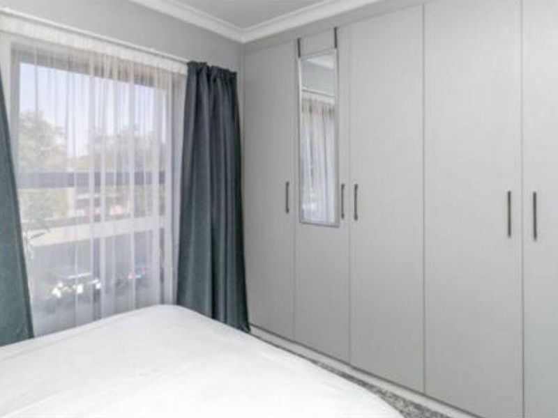 A bedroom featuring neutral-toned built-in cupboards with an integrated mirror and large window providing natural light.