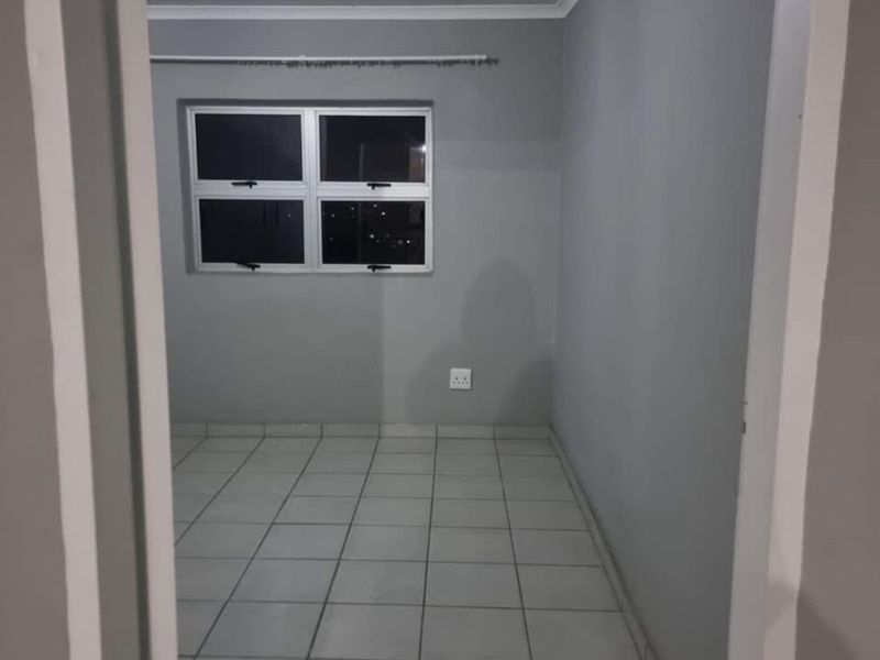 An empty bedroom featuring neutral grey walls, tiled flooring, and an aluminium-framed window, providing a clean and versatile space ready for furnishing.
