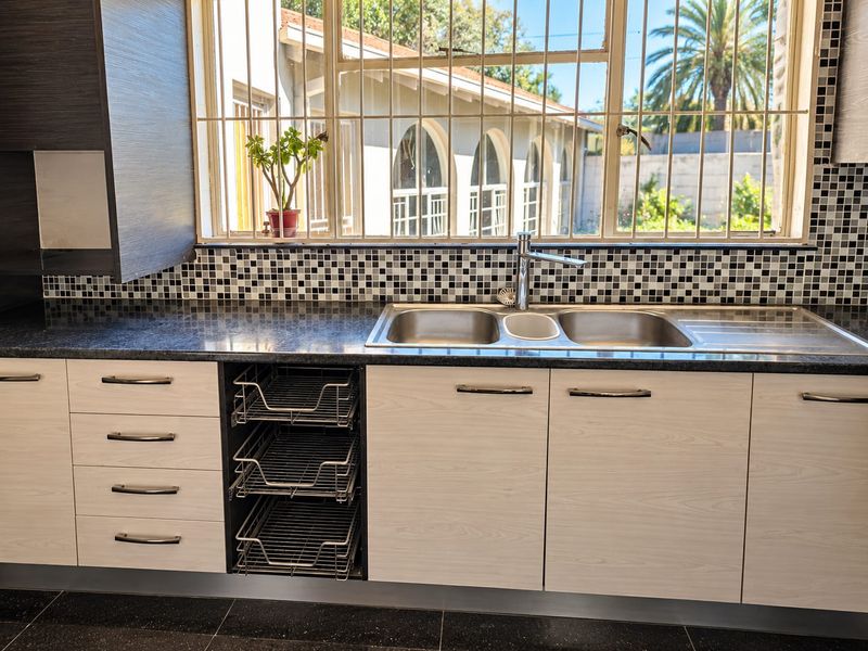 A well-maintained kitchen featuring modern laminate cabinetry, a double stainless steel sink, mosaic tile backsplash, and ample storage with pull-out wire baskets.