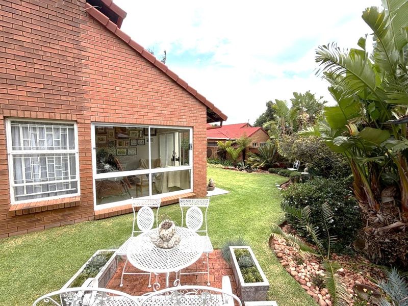 A well-maintained rear garden featuring a brick patio, lush landscaping, and a brick-faced house exterior with large sliding glass doors.