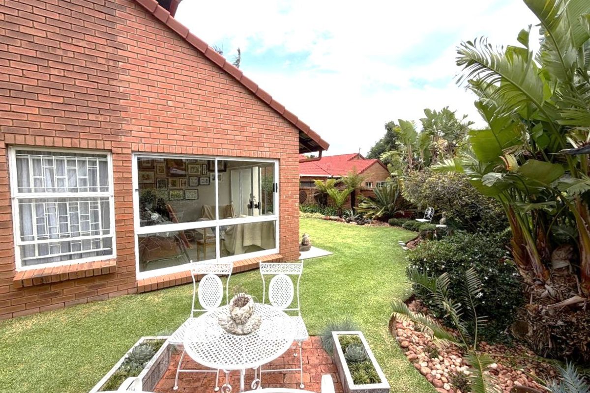A well-maintained rear garden featuring a brick patio, lush landscaping, and a brick-faced house exterior with large sliding glass doors.