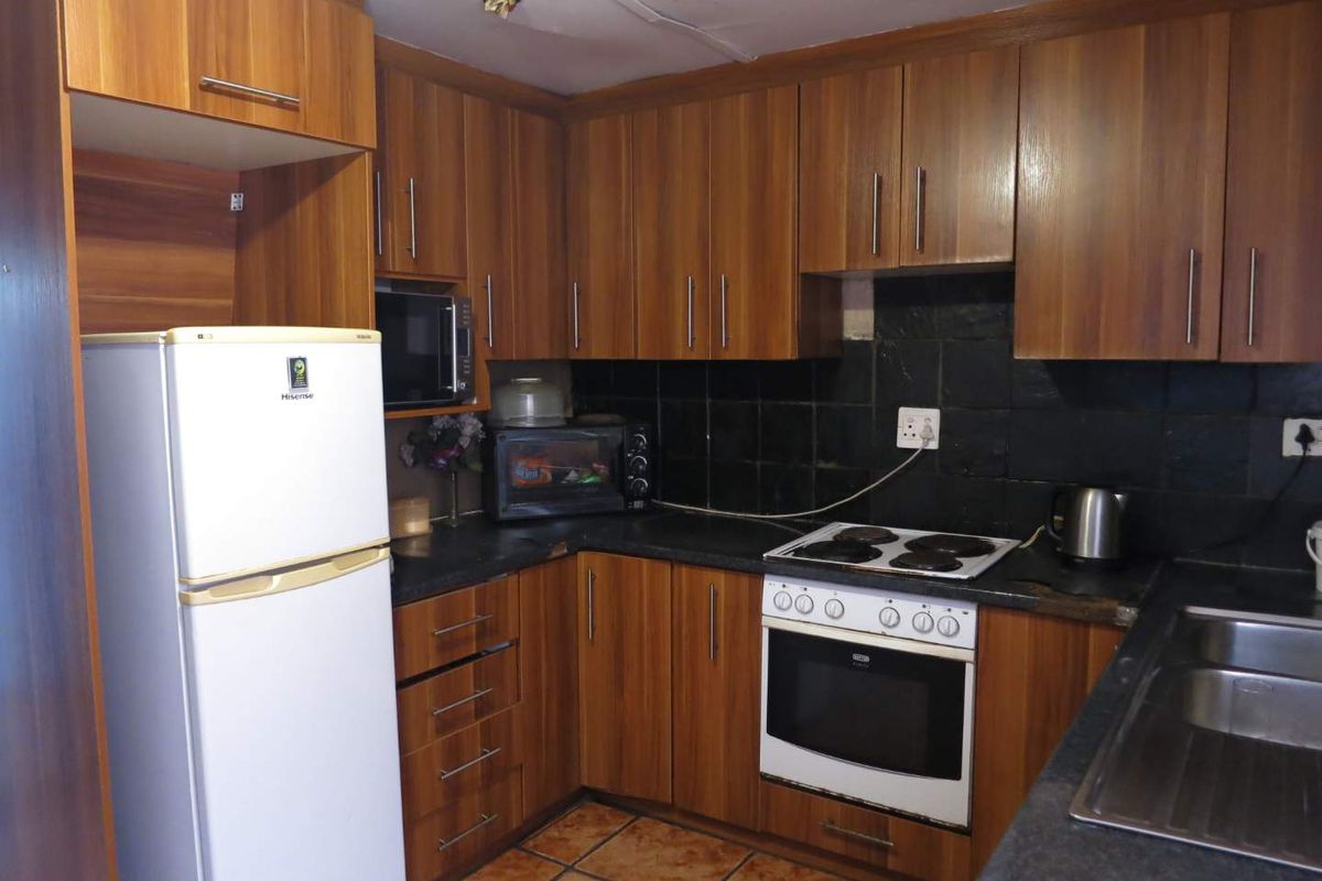 A functional kitchen featuring wood-look cabinetry, dark tiled splashbacks, a built-in oven, and a hob, providing a practical workspace for daily cooking.