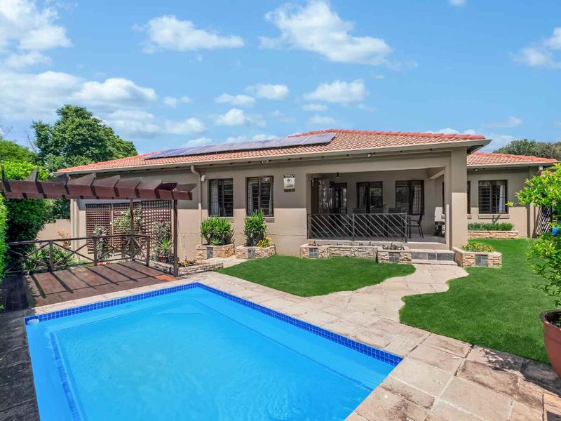 Rear view of the property featuring a swimming pool, paved patio area, wooden pergola, and solar panels installed on the tiled roof.