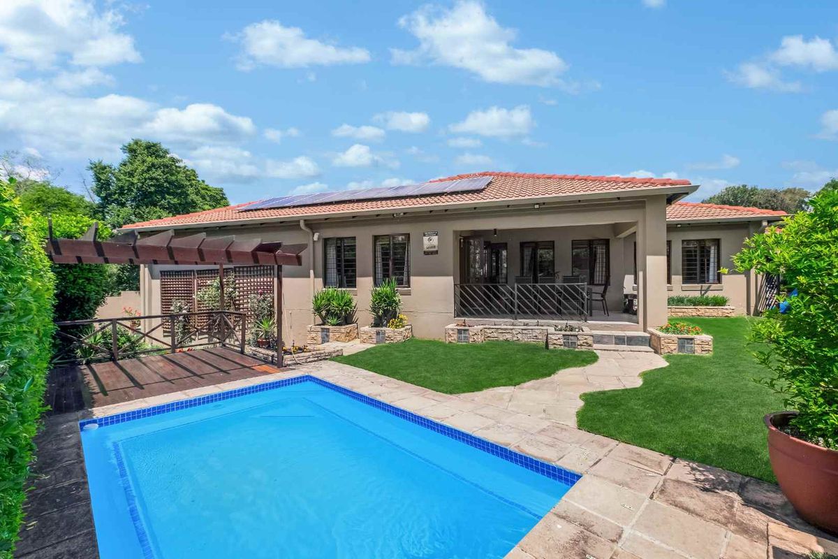 Rear view of the property featuring a swimming pool, paved patio area, wooden pergola, and solar panels installed on the tiled roof.