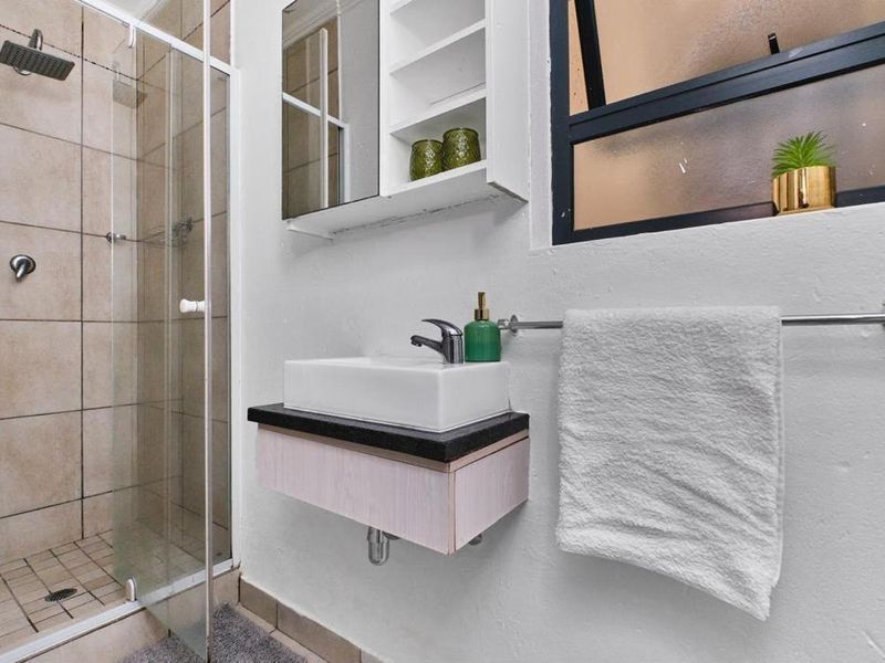 A modern bathroom featuring a glass-enclosed shower with a rain shower head, a wall-mounted vanity with a vessel sink, and a mirrored medicine cabinet.