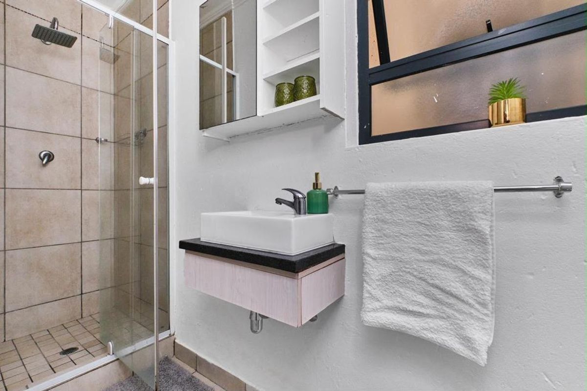 A modern bathroom featuring a glass-enclosed shower with a rain shower head, a wall-mounted vanity with a vessel sink, and a mirrored medicine cabinet.