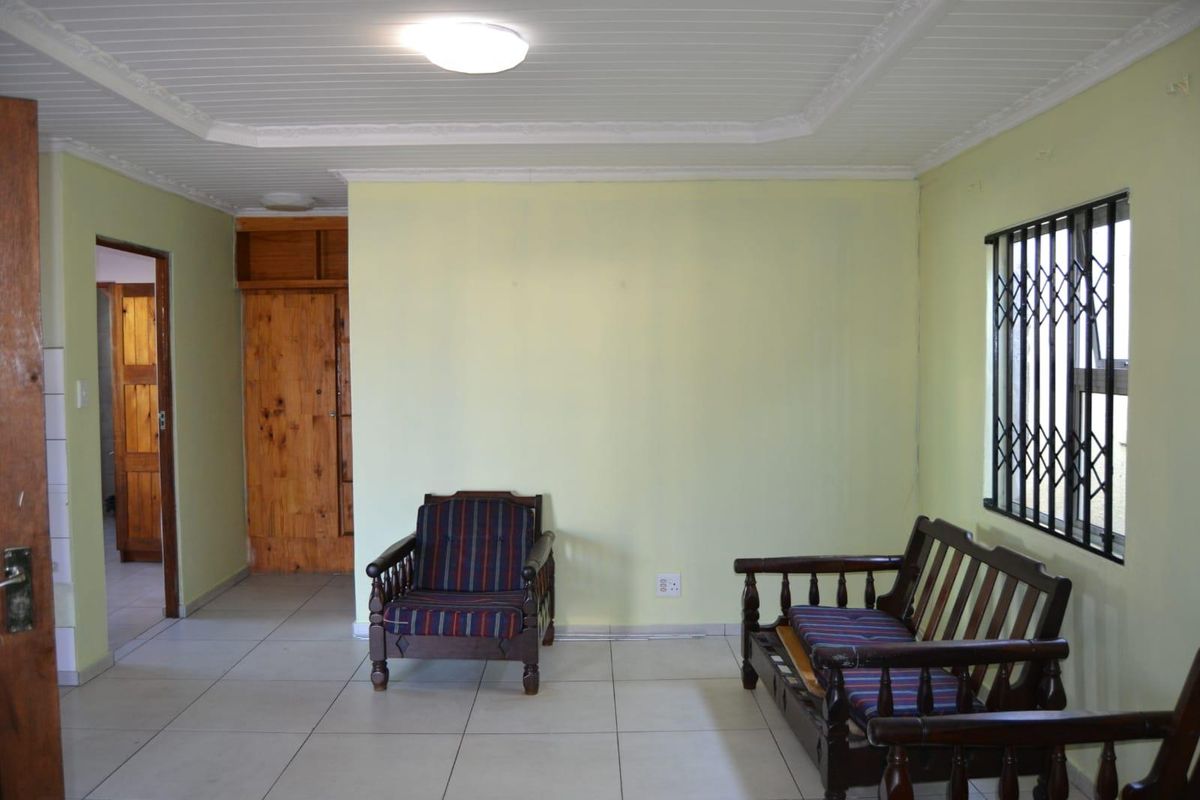 A living room featuring tiled flooring, a built-in wooden cupboard, and a window fitted with a security gate.