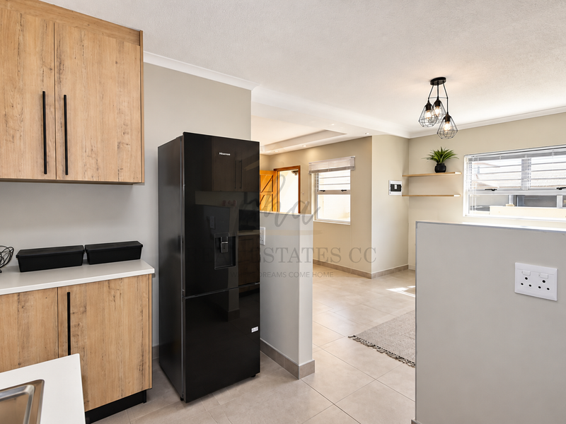 Modern kitchen featuring light wood-finish cabinetry, tiled flooring, and neutral walls, offering a clean and functional layout with integrated storage and contemporary lighting.