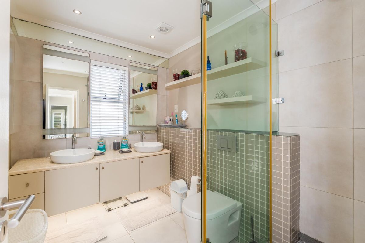 Modern bathroom featuring a double vanity with vessel sinks, a wall-mounted toilet, and a glass-enclosed shower with neutral tiling.