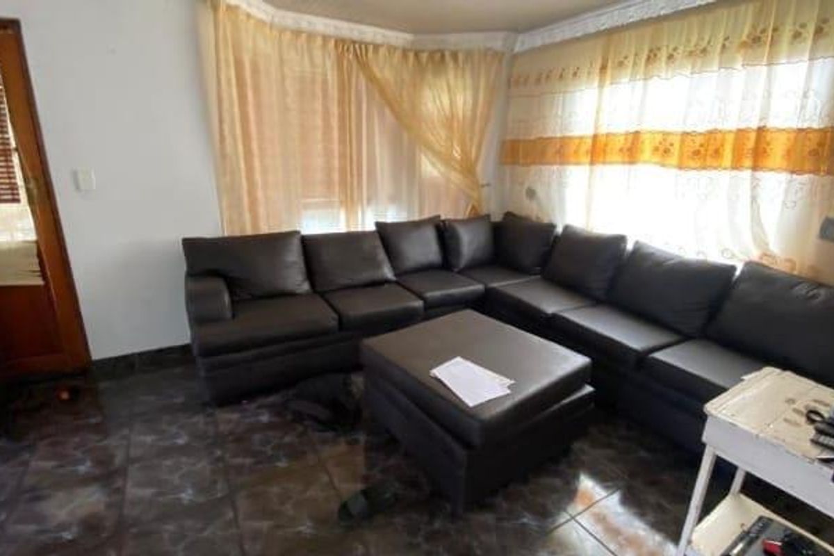 A living room area featuring dark tiled flooring and large windows with curtains, providing a functional space for relaxation.