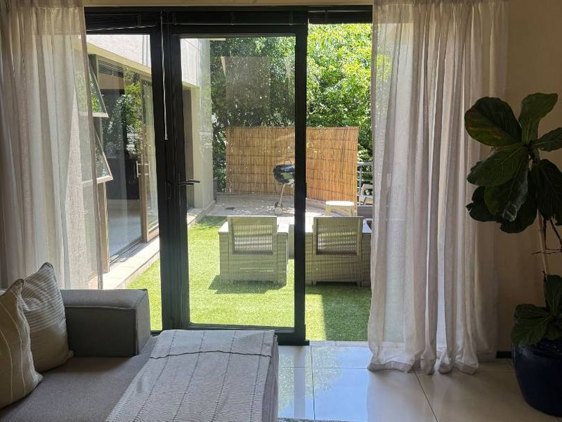 A bright living room featuring large sliding glass doors that provide seamless access to an outdoor patio and garden area.