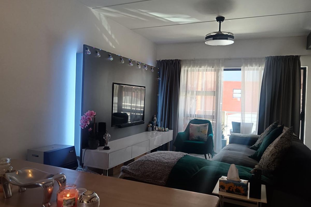A comfortable living room featuring a modern built-in media wall, ceiling fan, and large sliding glass doors providing access to the balcony.