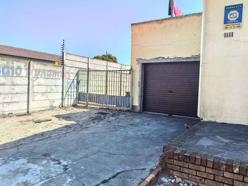 Exterior view of a townhouse garage featuring a roller shutter door, concrete driveway, and secure boundary walling with electric fencing.