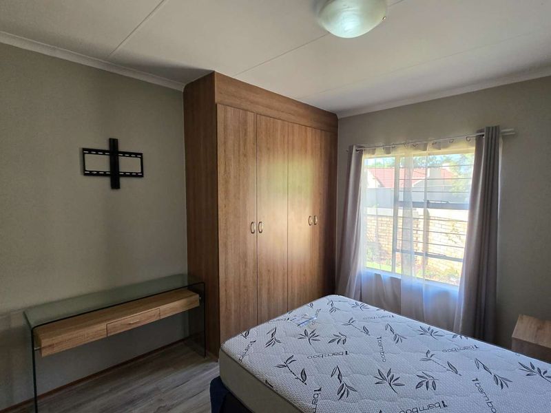 A bedroom featuring built-in wooden cupboards, laminate flooring, and natural light from a window.
