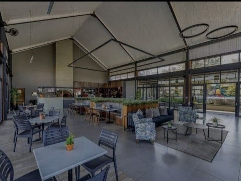 Spacious clubhouse area featuring vaulted ceilings with exposed beams, large glass doors for natural light, built-in pizza oven, and integrated banquette seating.