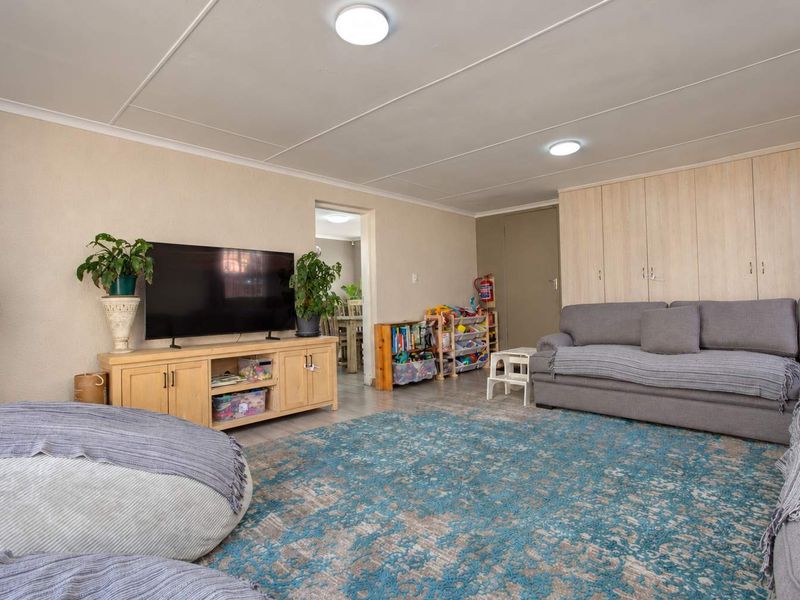 A spacious living room featuring neutral walls, tiled flooring, and extensive built-in storage cupboards, offering a functional and versatile family living space.
