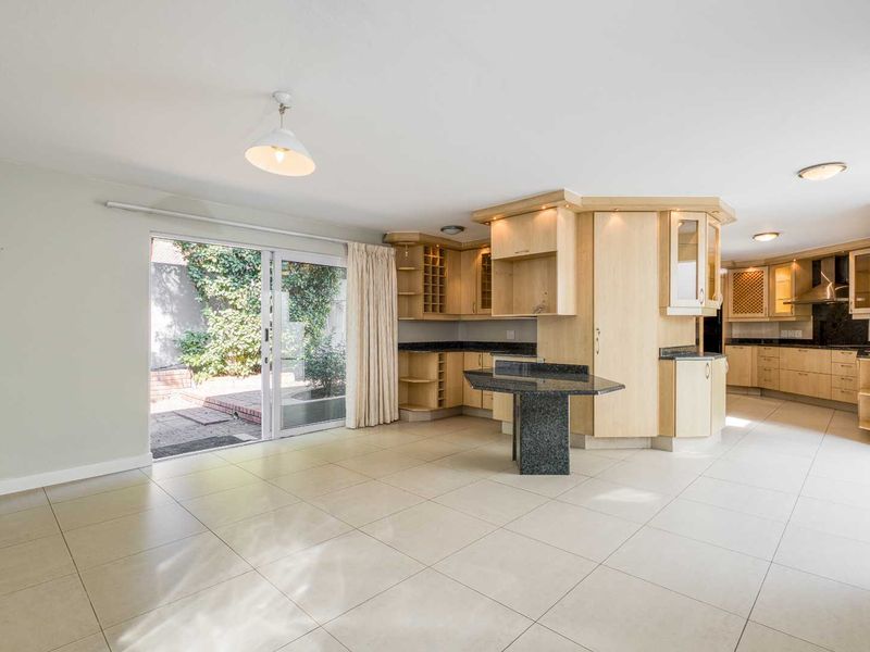 Spacious open-plan kitchen and living area featuring light wood cabinetry, granite countertops, tiled flooring, and direct access to a rear patio through sliding doors.
