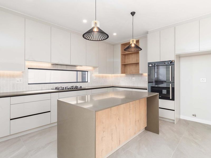 Modern kitchen featuring sleek white cabinetry, stone countertops, a central island, built-in oven, gas cooktop, and integrated lighting.