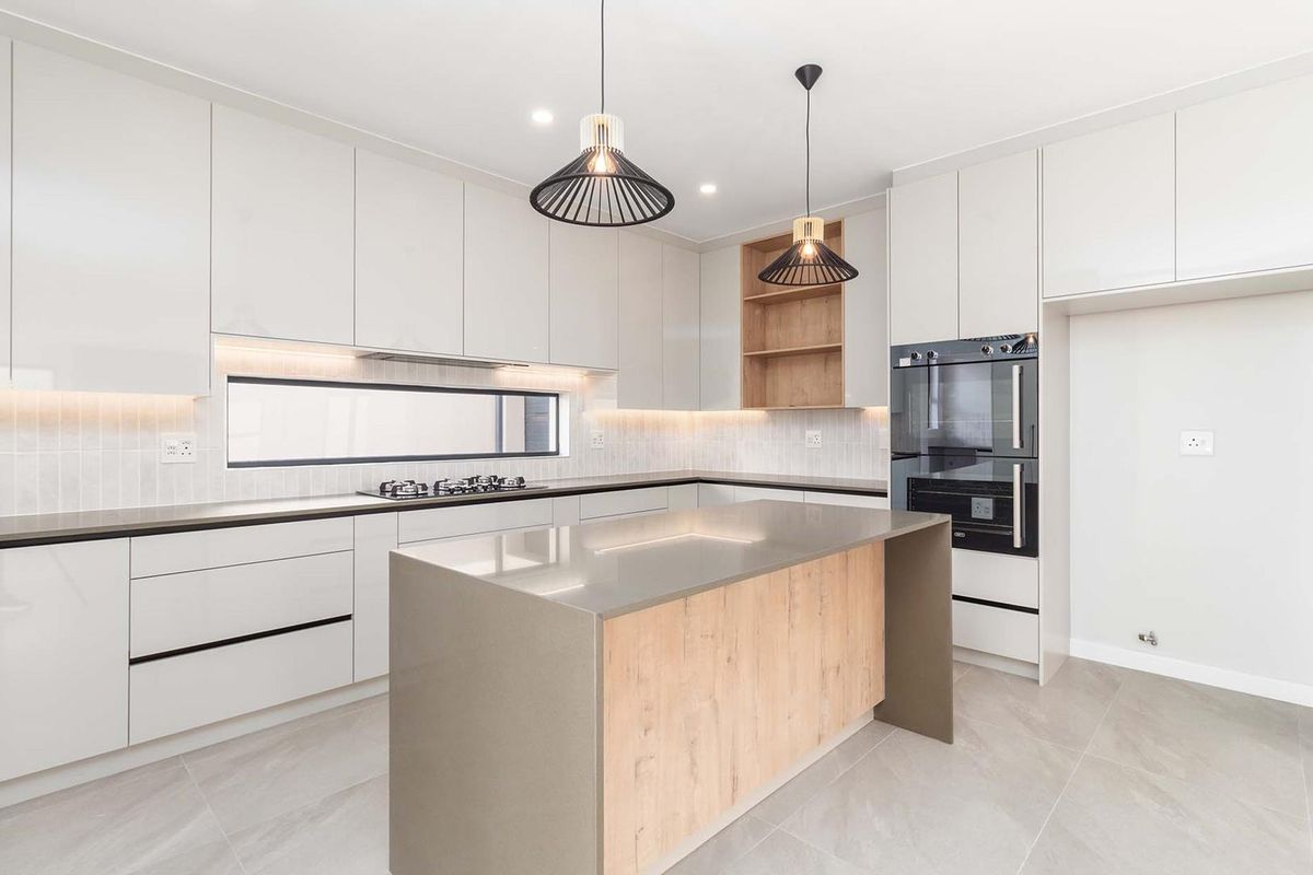 Modern kitchen featuring sleek white cabinetry, stone countertops, a central island, built-in oven, gas cooktop, and integrated lighting.