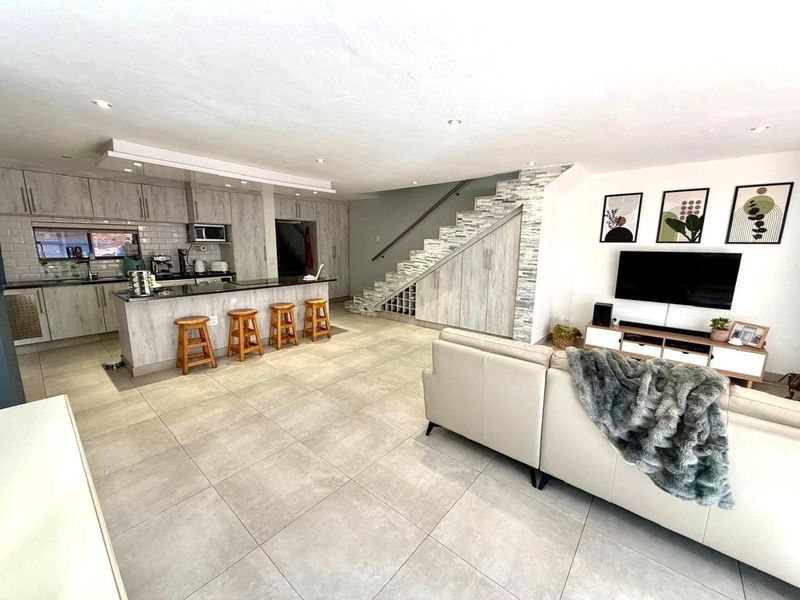 Open-plan living area featuring a modern kitchen with breakfast bar, tiled flooring, and a staircase with integrated storage and stone-cladding detail.