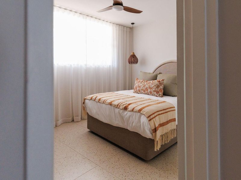 A well-lit bedroom featuring modern terrazzo flooring, a ceiling fan, and a stylish pendant light, viewed through a doorway.