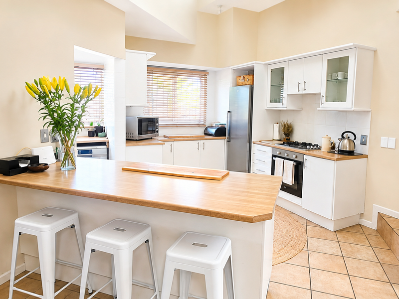 A bright, functional kitchen featuring white cabinetry, wooden countertops, a gas hob, and a convenient breakfast bar area with tiled flooring.