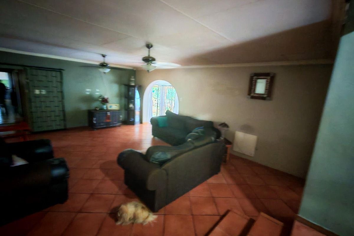 Spacious living area featuring terracotta floor tiles, dual ceiling fans, and an arched doorway leading to the exterior.