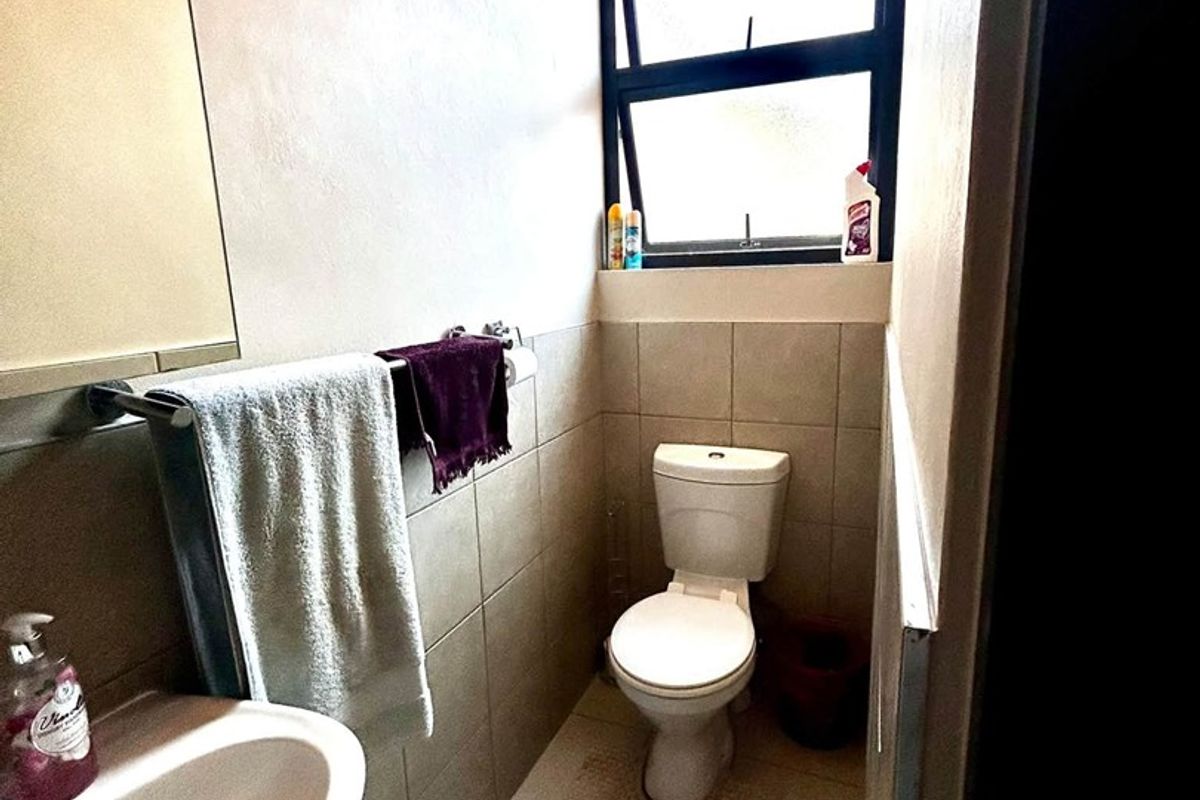 A compact bathroom featuring a pedestal basin, toilet, and neutral wall and floor tiling with a top-hung window for natural light.