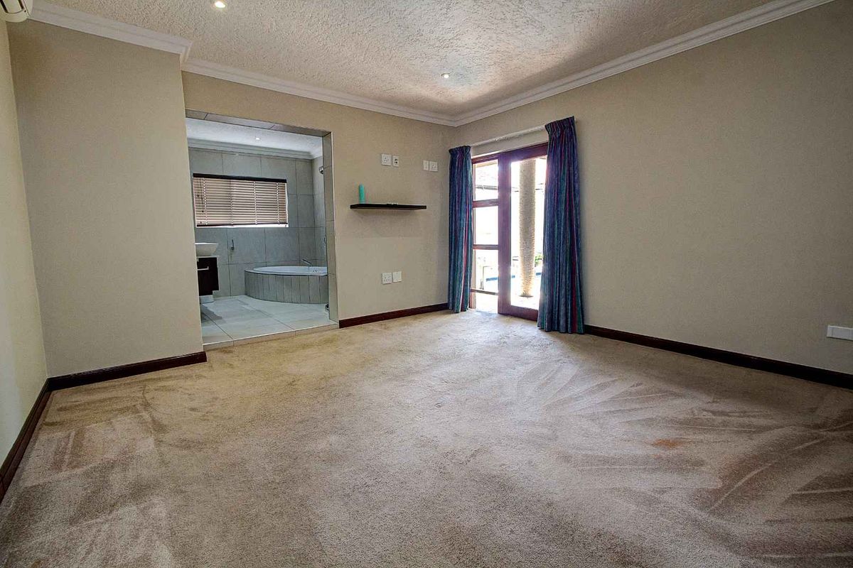 Spacious bedroom featuring neutral walls, plush carpeting, and direct access to an en-suite bathroom and outdoor area through glass doors.