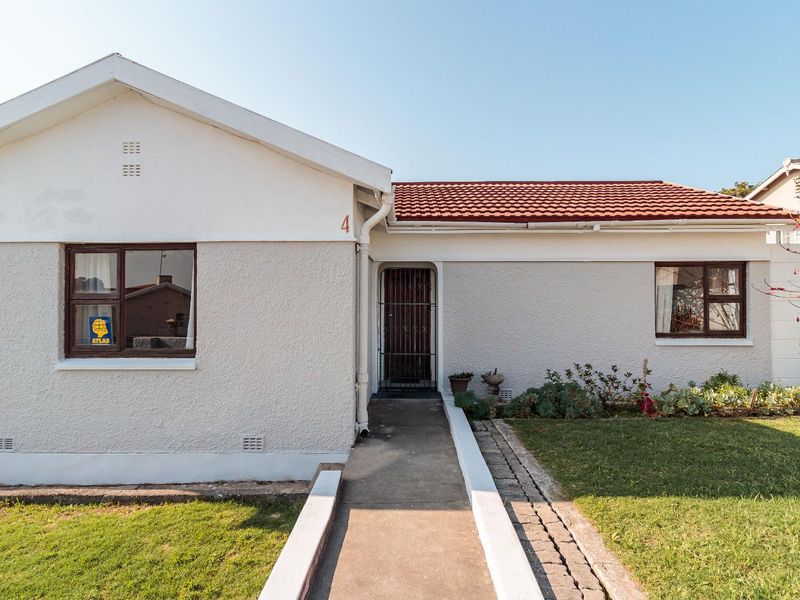 Front elevation of a single-story house featuring a tiled roof, concrete walkway, and secure entrance gate with established garden area.