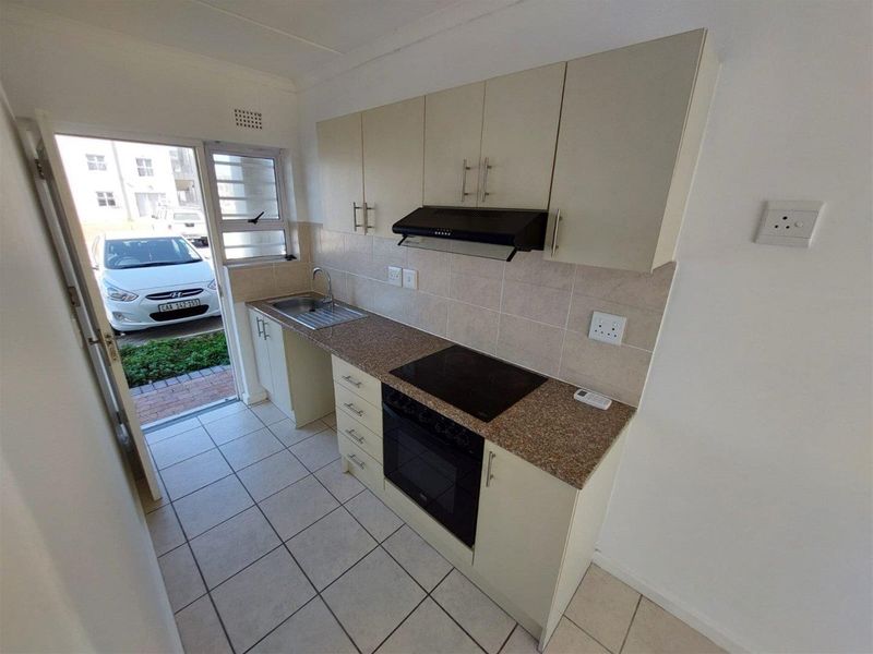 A compact, functional kitchen featuring built-in cabinetry, granite countertops, an electric hob, oven, and extractor fan, with direct access to the exterior.