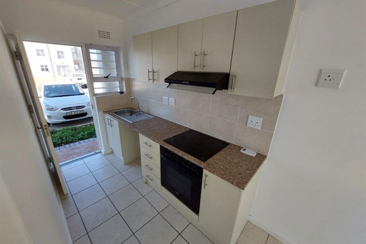 A compact, functional kitchen featuring built-in cabinetry, granite countertops, an electric hob, oven, and extractor fan, with direct access to the exterior.