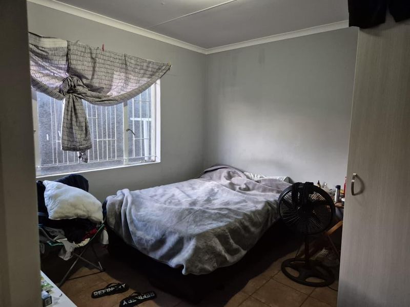 A bedroom featuring a built-in cupboard, tiled flooring, and a window with security bars, requiring minor cosmetic updates to the wall finishes.
