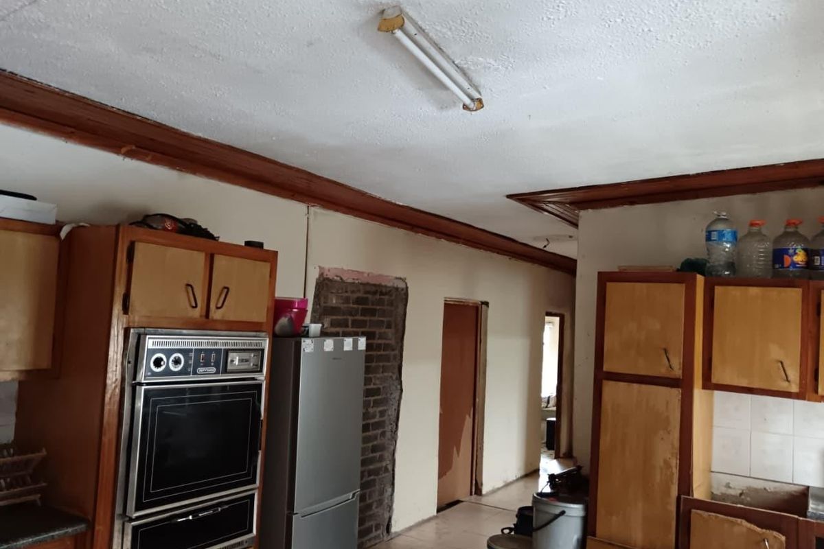 A dated kitchen featuring original wooden cabinetry, a built-in oven, and exposed brickwork, requiring significant renovation and cosmetic updates to modernize the space.