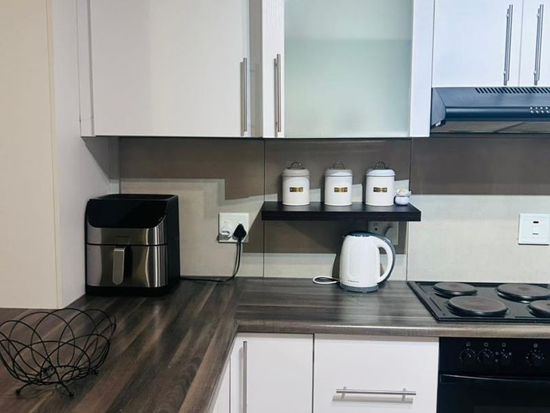 A modern kitchen featuring white cabinetry, dark laminate countertops, a built-in oven, electric hob, and an extractor fan with a tiled backsplash.