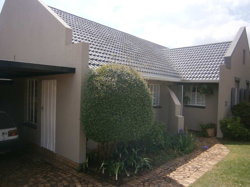 Front elevation of a townhouse featuring a tiled roof, carport, and paved walkway leading to the entrance.