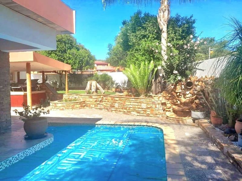Outdoor pool area featuring a covered patio, stone retaining walls, and a decorative stone water feature in a landscaped garden setting.