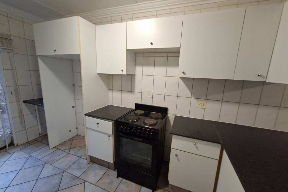 A dated kitchen featuring white cabinetry, dark countertops, and tiled flooring, offering a functional layout ready for modernization and cosmetic updates.
