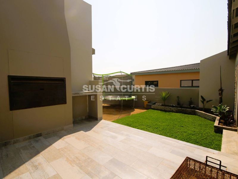 A covered patio area featuring a built-in braai, tiled flooring, and a view of the private garden.
