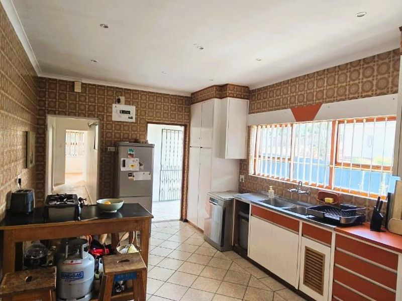 A functional kitchen featuring extensive wall tiling, built-in cabinetry, and a double basin sink, offering potential for a modern renovation.