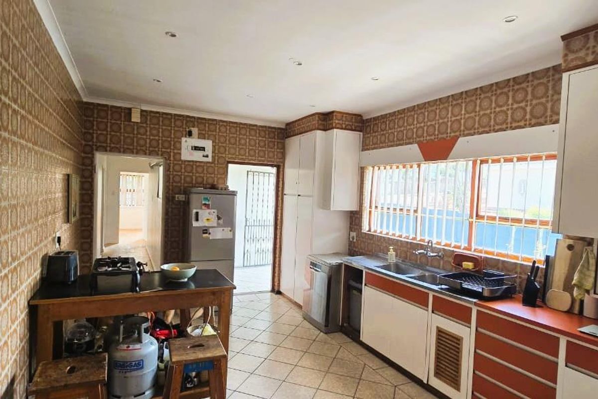 A functional kitchen featuring extensive wall tiling, built-in cabinetry, and a double basin sink, offering potential for a modern renovation.
