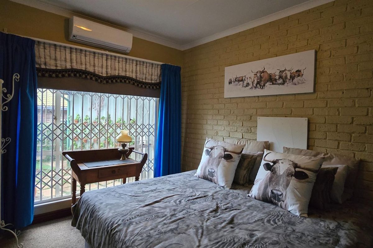 A bedroom featuring an exposed brick wall, carpeted flooring, and a wall-mounted split-system air conditioner for climate control.